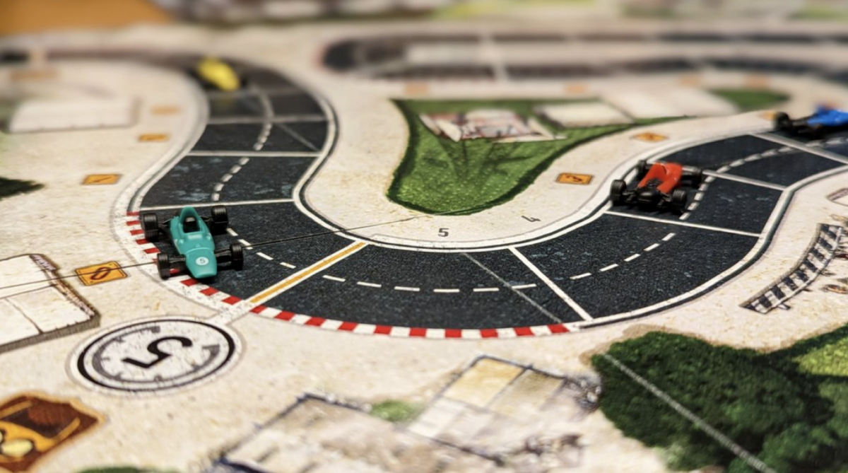Brettspill med en gul, grønn og rød formel 1 bil som kjører i helt OK fart gjennom en sving.